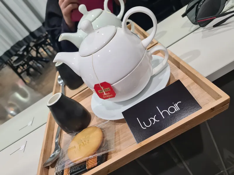 A pot of tea and biscuit on a timber tray with a lux hair card